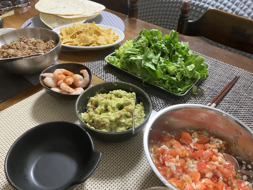 自宅で作ったタコスパーティー。トルティーヤ、ワカモレ、サルサソース、ひき肉、エビ、レタスを並べた食卓。