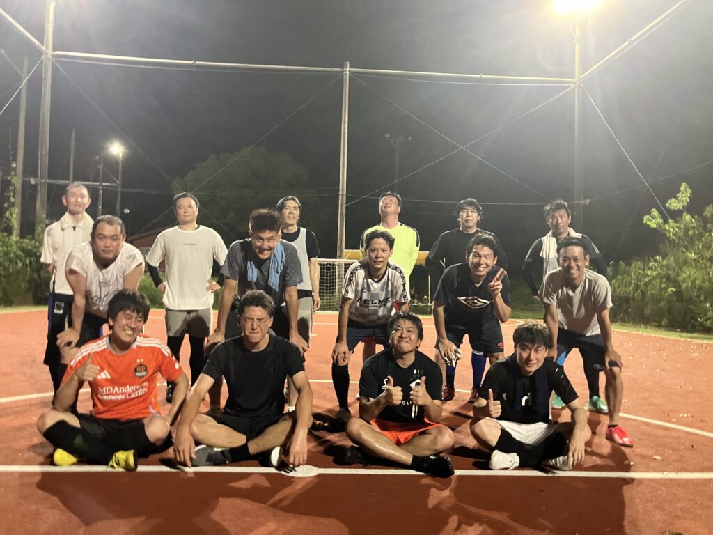 名古屋オーシャンズフットサルスクール桑名校のスクール生お父さん対象「ゲームナイト」参加者による集合写真。ナイターのフットサルコートで試合後に笑顔で記念撮影する参加者。
